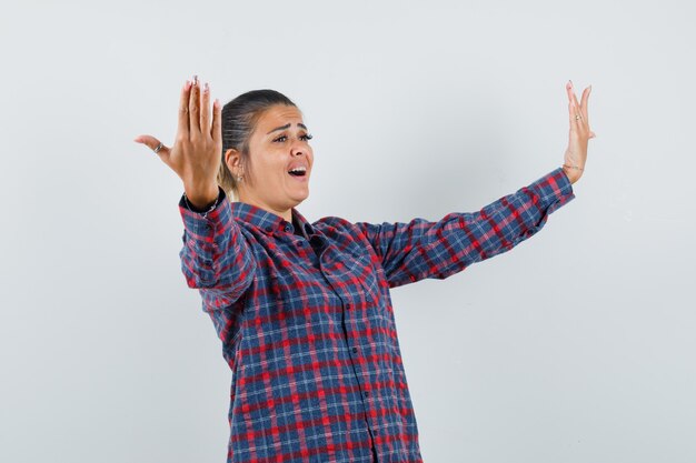 Young woman stretching hands like inviting to come in checked shirt and looking happy , front view.