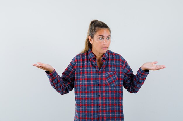 Foto gratuita giovane donna che allunga le mani in modo interrogativo in camicia a quadri e sembra perplessa