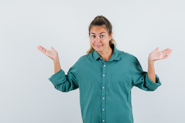 Young woman stretching hands in questioning manner in green blouse and looking cute