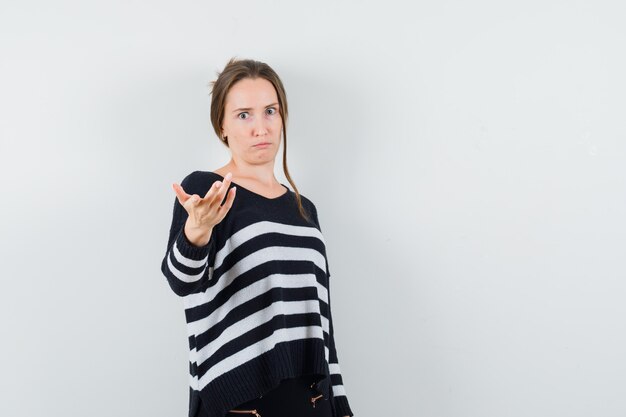 Young woman stretching hands toward front in black blouse and black pants and looking surprised