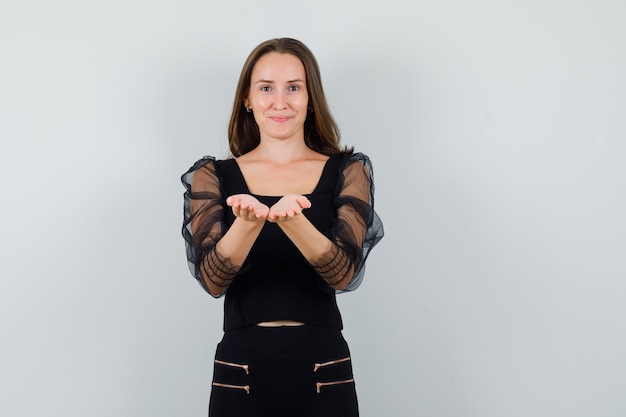 Free photo young woman stretching hands towards camera in black blouse and black pants and looking attractive. front view.