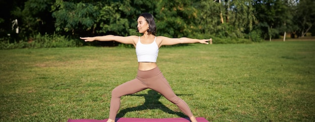 Free photo young woman stretching her body workout and doing yoga in park standing on rubber mat in fitness