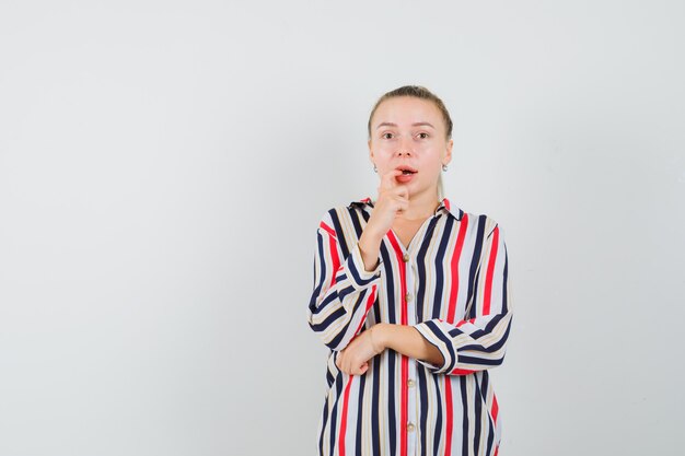 Young woman in striped blouse biting her finger and looking frightened