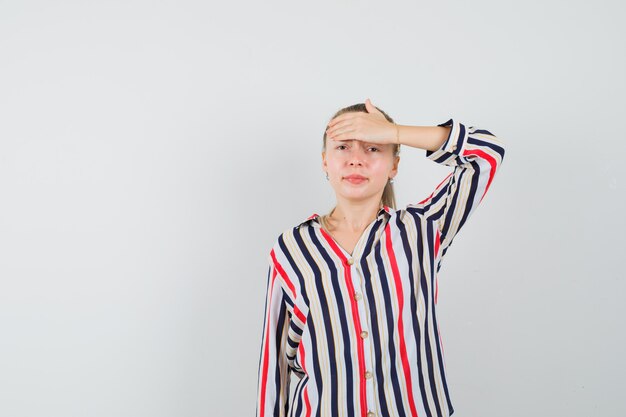 Young woman in striped blouse covering her forehead with one head and looking tired