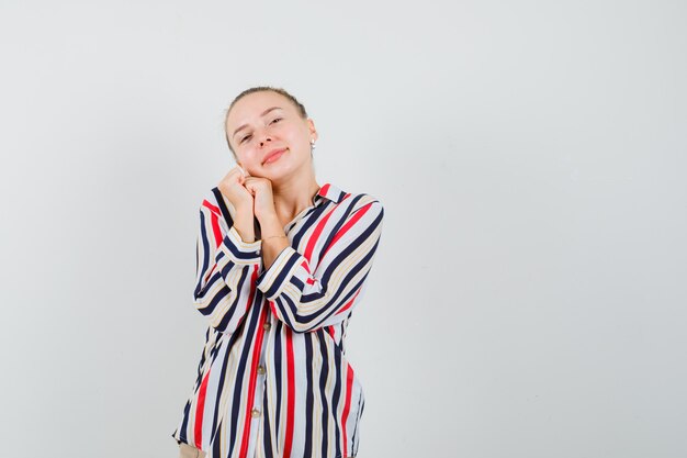 Young woman in striped blouse leaning her cheek on palms and looking pretty