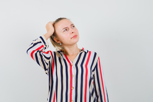 Young woman in striped blouse put her head on head and looking indecisive