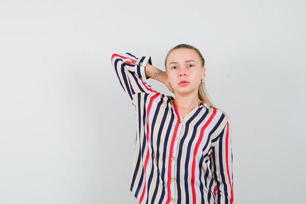 Young woman in striped blouse putting her arm behind head and looking pretty