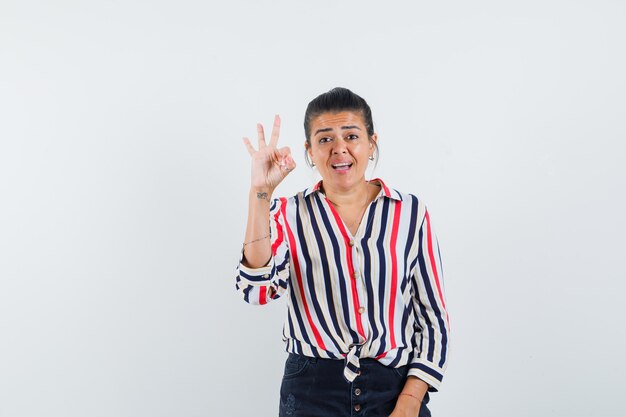 Young woman in striped blouse showing ok sign and looking optimistic