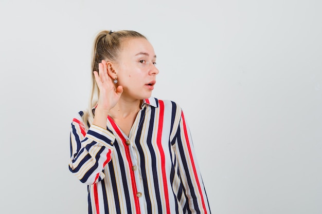 Young woman in striped blouse trying to hear something and looking curious