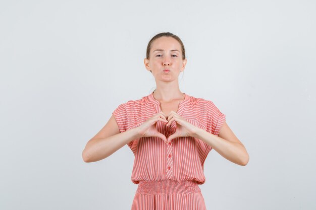 Young woman in striped dress making heart shape with hands , front view.