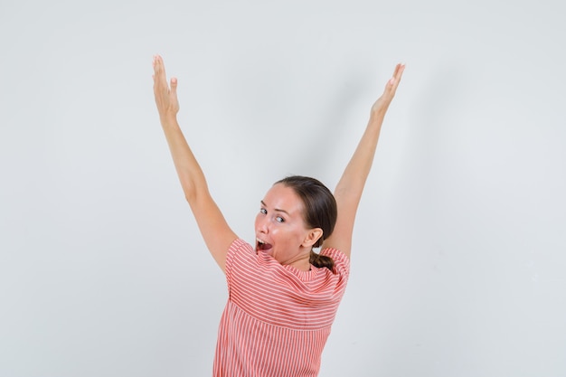 Foto gratuita giovane donna in abito a righe alzando le braccia mentre guarda indietro e sembra felice, vista posteriore.