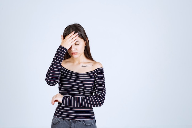 Young woman in striped shirt holding her head because of headache