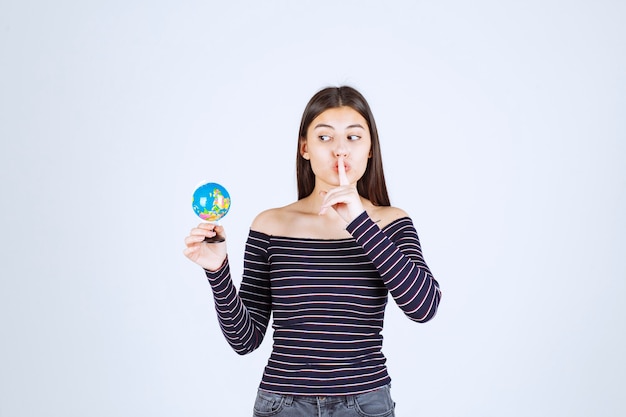 Young woman in striped shirt holding a mini globe and asking for silence
