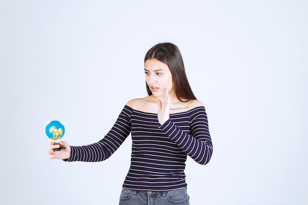 Giovane donna in camicia a righe che tiene un mini globo e vuole fermarlo