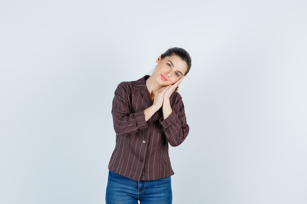 Молодая женщина в полосатой рубашке, джинсах, опираясь щекой на ладони как подушку и выглядящей очаровательно, вид спереди.