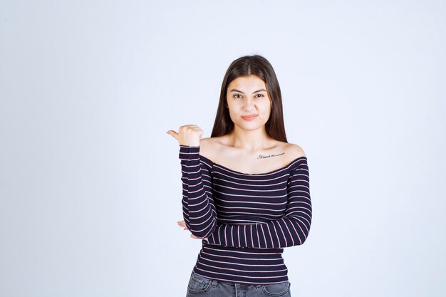 Young woman in striped shirt pointing at something behind