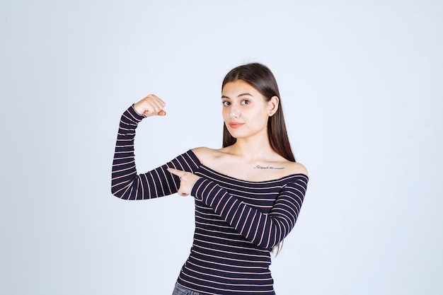 Young woman in striped shirt showing her arm muscle and fist