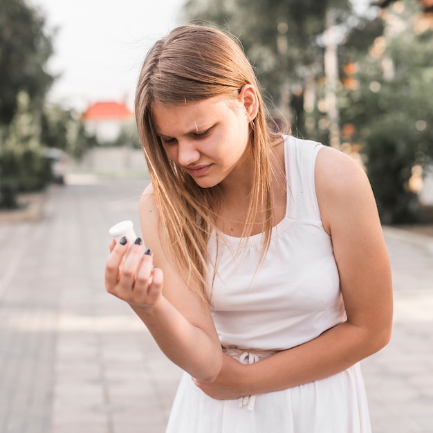 Young woman suffering from stomach pain holding pill bottle