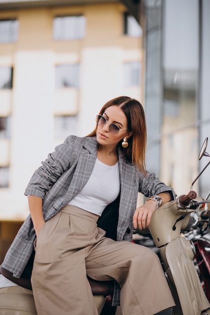 Free photo young woman in suit standing by the scooter