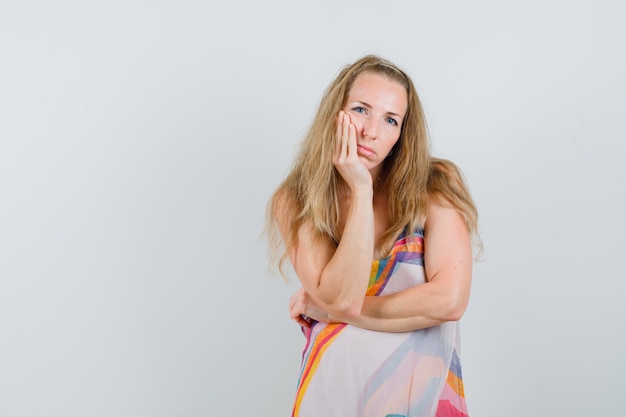 Young woman in summer dress leaning cheek on palm and looking thoughtful 