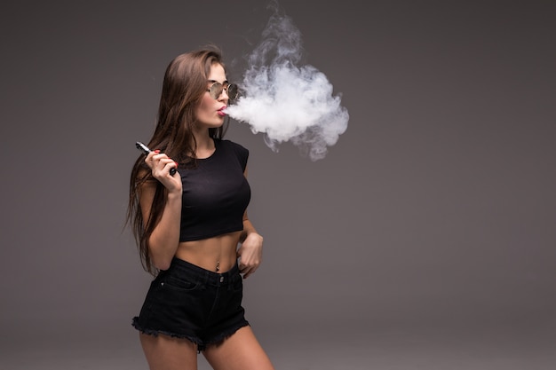 サングラスとvapingと灰色の壁に電子タバコの煙を吹いて黒い服の若い女性