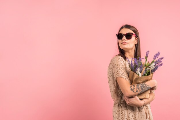 サングラスの花を持つバッグを保持している若い女性