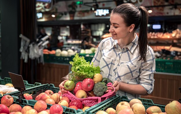 Молодая женщина в супермаркете с овощами и фруктами покупает продукты