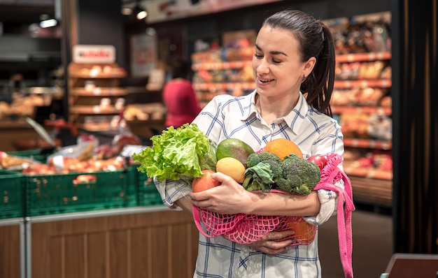 Молодая женщина в супермаркете с овощами и фруктами покупает продукты