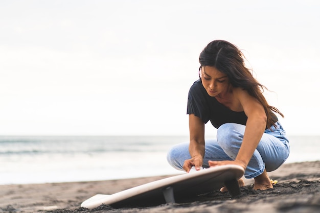 Giovane donna surfista preparare una tavola da surf sull'oceano ceretta donna con tavola da surf sull'oceano sport acquatici stile di vita attivo