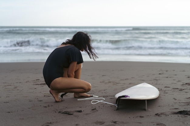 Foto gratuita giovane donna surfista preparare una tavola da surf sull'oceano ceretta donna con tavola da surf sull'oceano sport acquatici stile di vita attivo