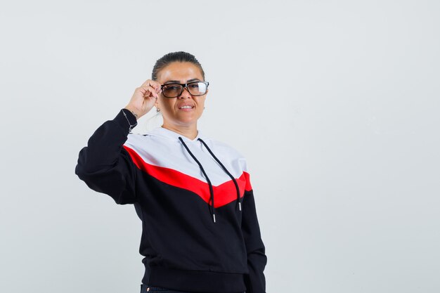 Young woman in sweater and black jean holding glasses with one hand and looking happy , front view.