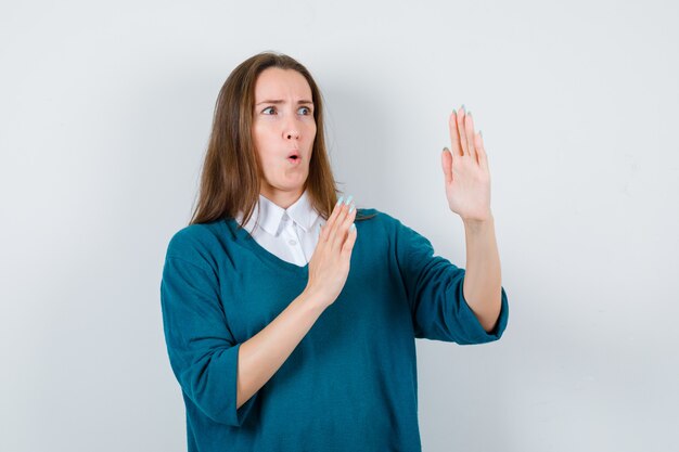 Young woman in sweater over white shirt showing karate chop gesture and looking scared , front view.