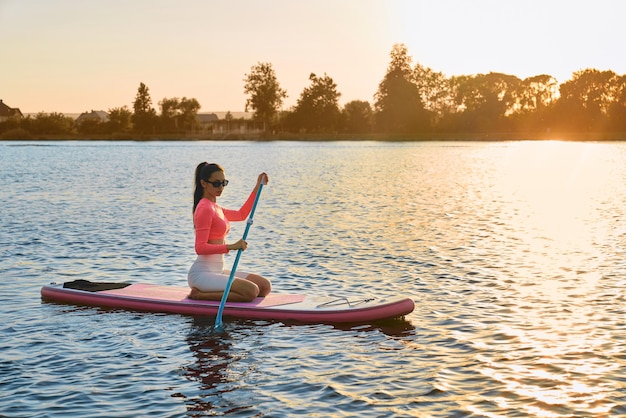 Free photo young woman swimming on sup board during sunset