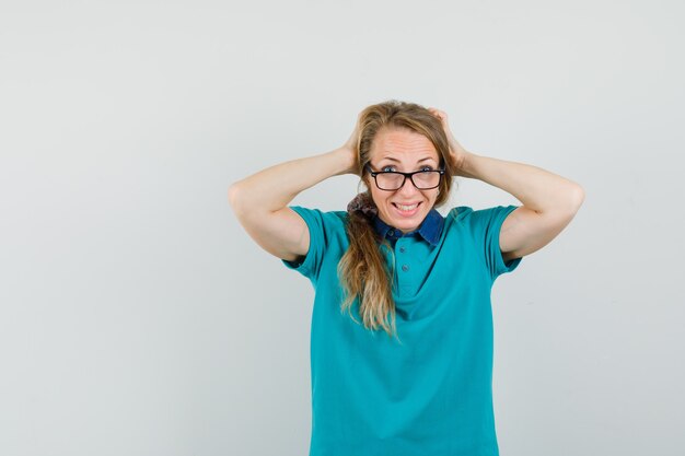 Young woman in t-shirt clasping head with hands and looking merry 