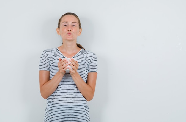 Foto gratuita giovane donna in t-shirt che tiene tazza di tè con labbra arrotondate, vista frontale.