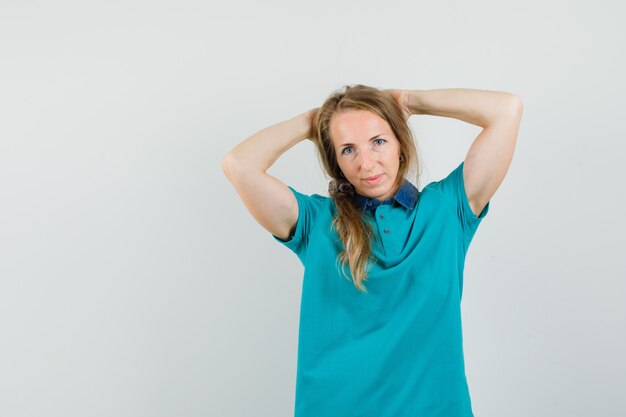 Young woman in t-shirt holding hands behind head and looking confident 