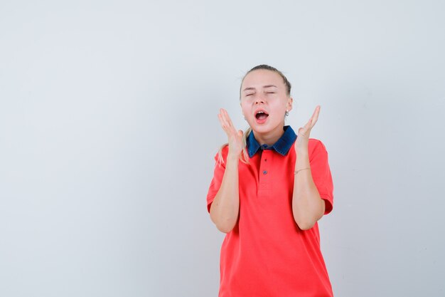 Young woman in t-shirt holding hands near face while screaming and looking excited