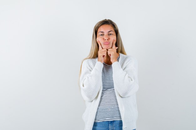 Young woman in t-shirt, jacket keeping fingers on cheeks and looking gloomy , front view.