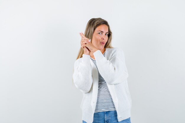 Young woman in t-shirt, jacket showing gun gesture and looking confident , front view.