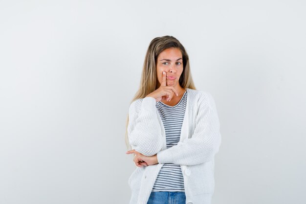 Young woman in t-shirt, jacket standing in thinking pose and looking intelligent , front view.