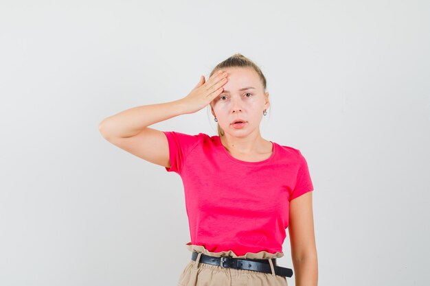 Young woman in t-shirt and pants holding hand on forehead and looking mournful