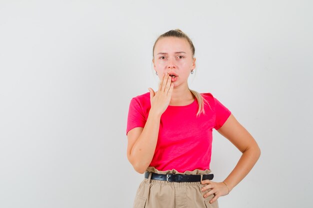 開いた口に手をつないで、物欲しそうに見えるTシャツとズボンの若い女性