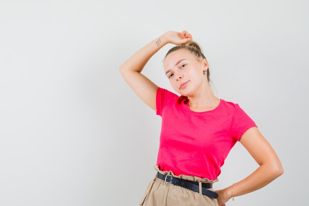 Young woman in t-shirt and pants posing with raised hand on head and looking stunning