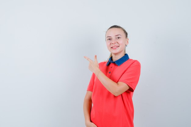 Young woman in t-shirt pointing at upper left side and looking glad