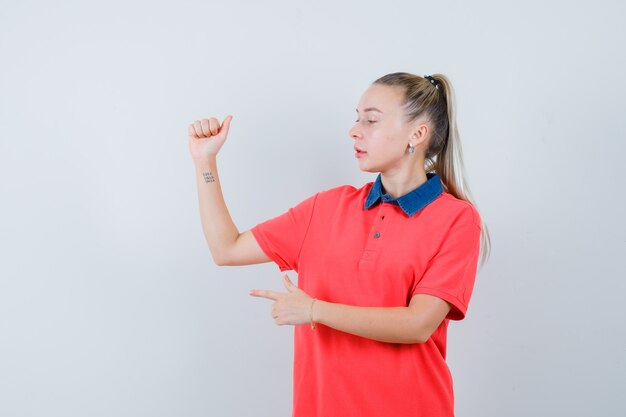 Молодая женщина в футболке поднимает руку, указывая в сторону и выглядит сосредоточенной