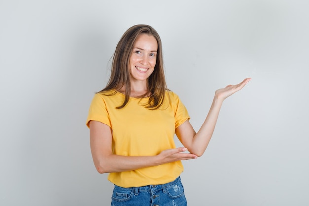 Young woman in t-shirt, shorts inviting to come with hands and looking cheerful