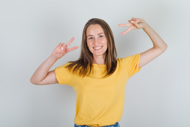 Young woman in t-shirt, shorts showing peace gesture and looking jolly