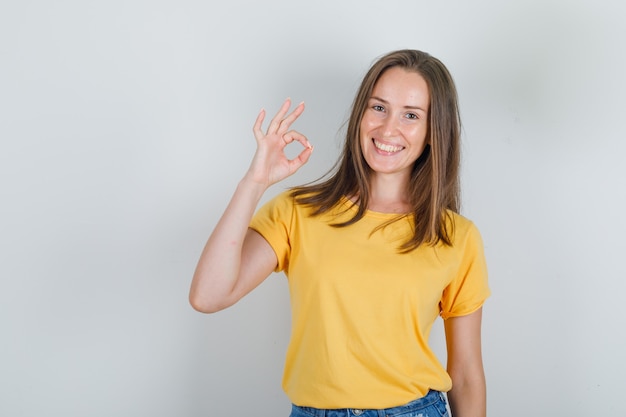 Giovane donna in maglietta, pantaloncini sorridenti e mostrando segno ok