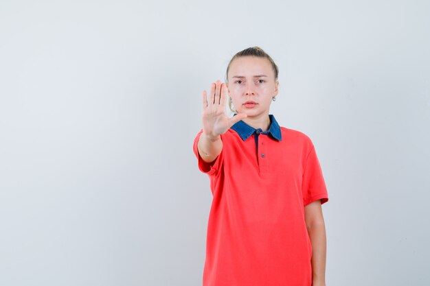 Young woman in t-shirt showing stop gesture and looking serious