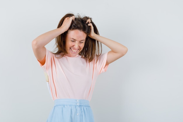 Young woman in t-shirt, skirt holding hands in hair and looking lucky , front view.